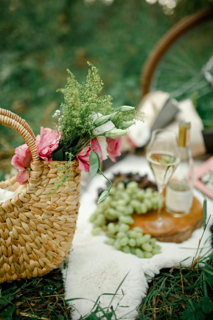 a basket with flowers beside grapes and white wine